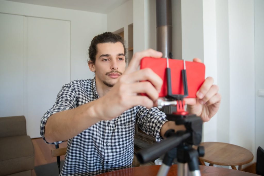 pexels photo 7514825 Confident young man adjusting smartphone on tripod for home vlogging setup.